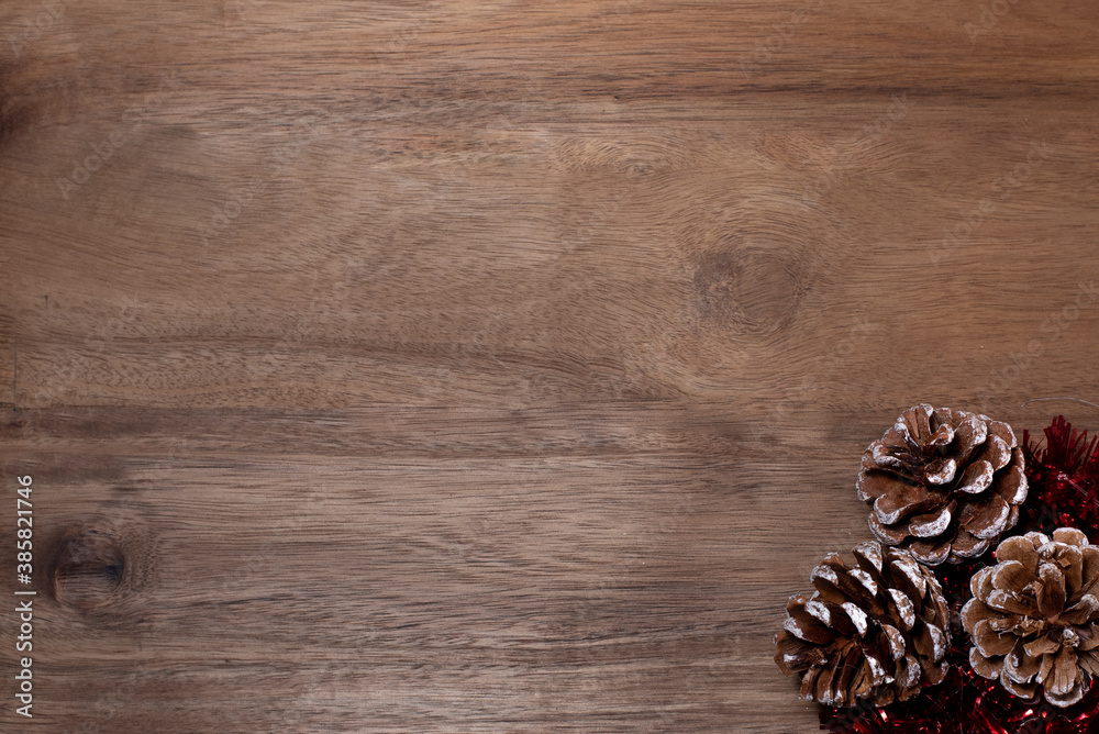 Pine cones with red tinsel on the wooden background.