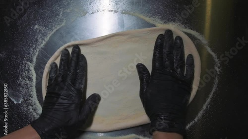 Chef in black gloves prepares pizza dough