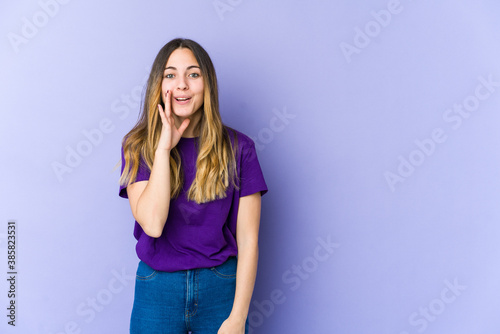 Young caucasian woman isolated on purple background shouts loud, keeps eyes opened and hands tense.