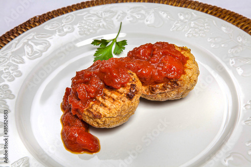 Grilled vegetarian dumplings topped with tomato sauce on a white plate with embossed edge