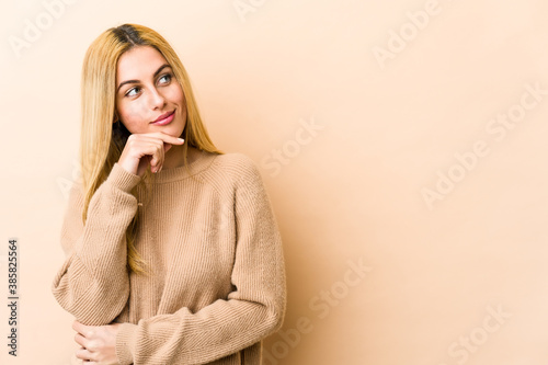 Young blonde caucasian woman looking sideways with doubtful and skeptical expression.