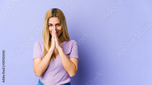 Young blonde caucasian woman holding hands in pray near mouth, feels confident.