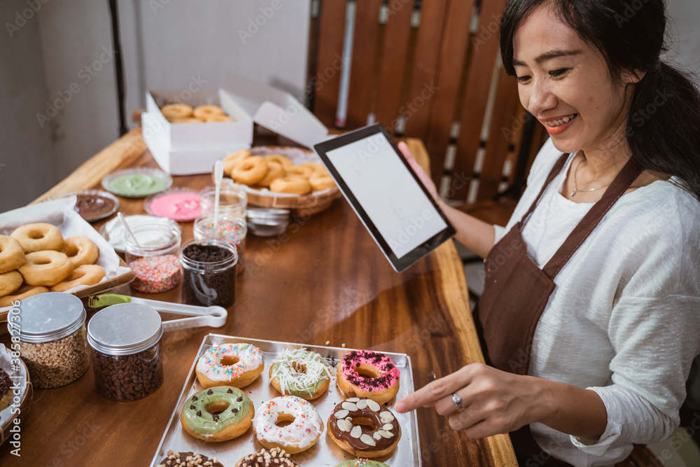 female chef wearing an apron points to a donut while using a tablet while sitting in the kitchen