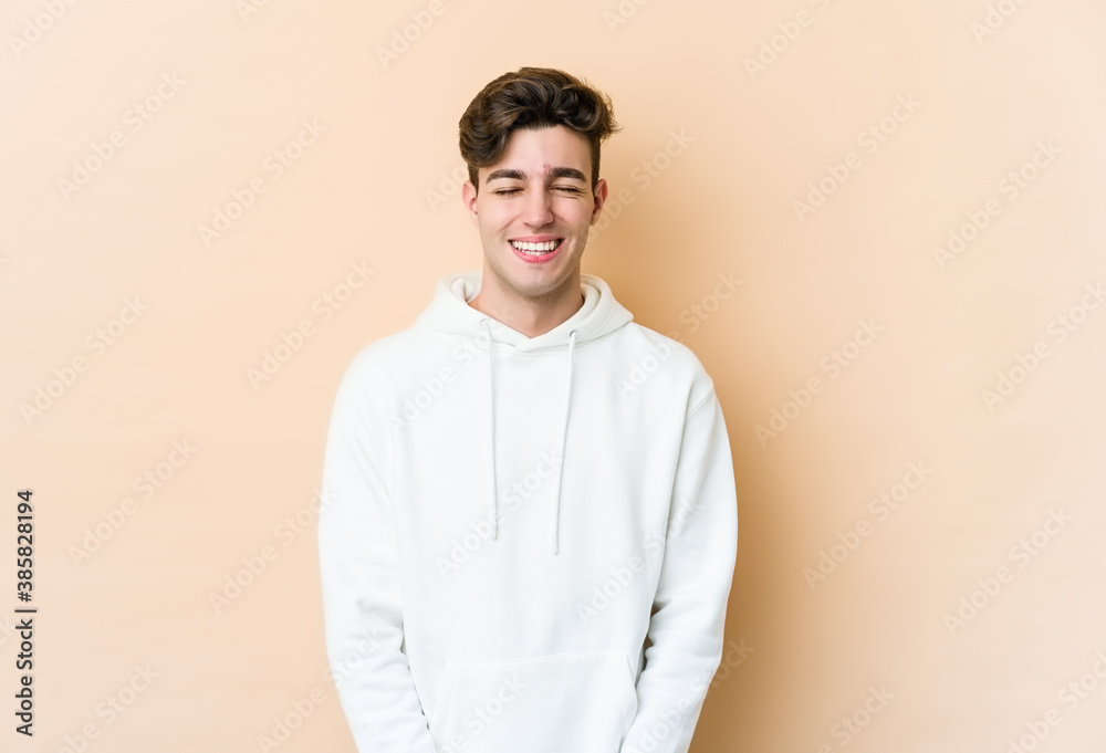 Young caucasian man isolated on beige background laughs and closes eyes, feels relaxed and happy. Young caucasian man isolated on beige background laughs and closes eyes, feels relaxed and happy.