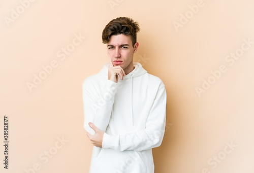 Young caucasian man isolated on beige background contemplating, planning a strategy, thinking about the way of a business.