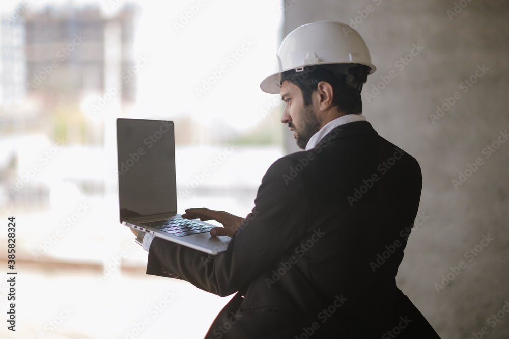 Man in suit and safety helmet works on laptop Man in suit and safety helmet works on laptop