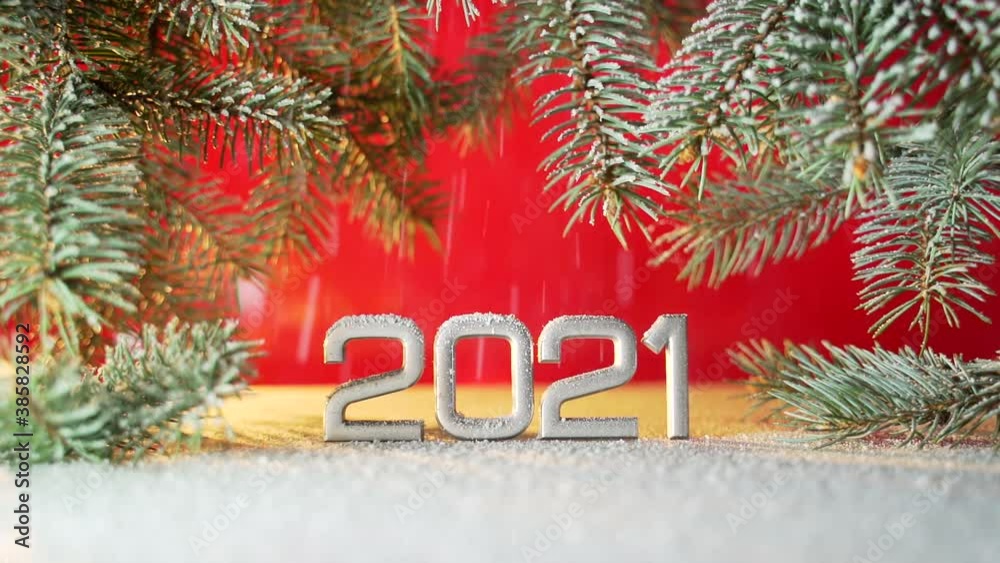 Close up. Date new year figures 2021. It's snowing. Snow falls. on the branches of a Christmas tree or pine on a red background. Macro silver inscription. The date is reflected. copy space for text. Close up. Date new year figures 2021. It's snowing. Snow falls. on the branches of a Christmas tree or pine on a red background. Macro silver inscription. The date is reflected. copy space for text.