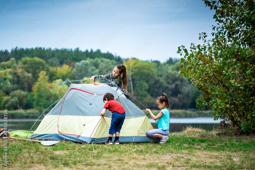 Children pitching a tent on the campsite near lake - obrazy, fototapety, plakaty 