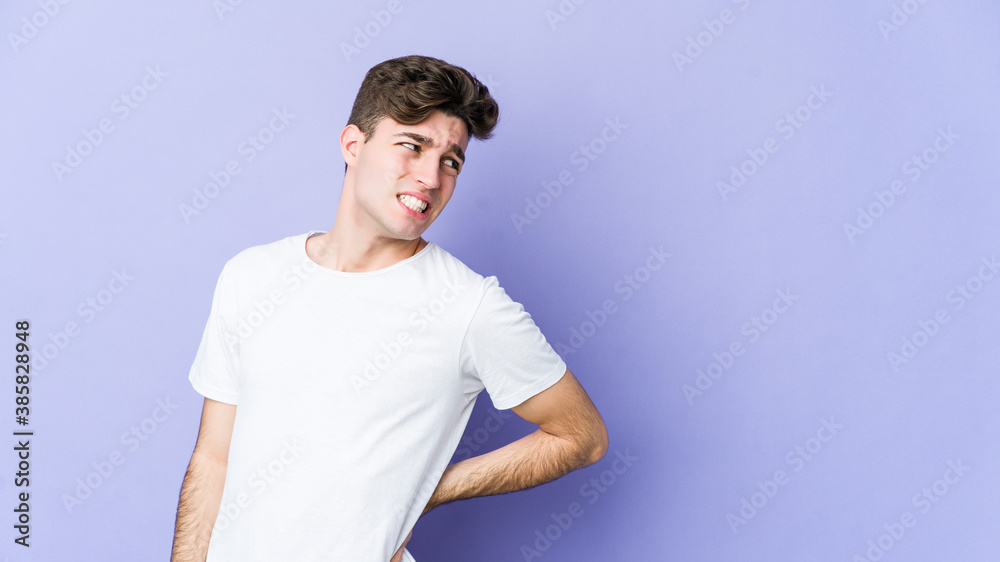 Young caucasian man isolated on purple background suffering a back pain.