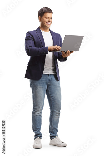 Full length portrait of a young man standing and working on a laptop computer