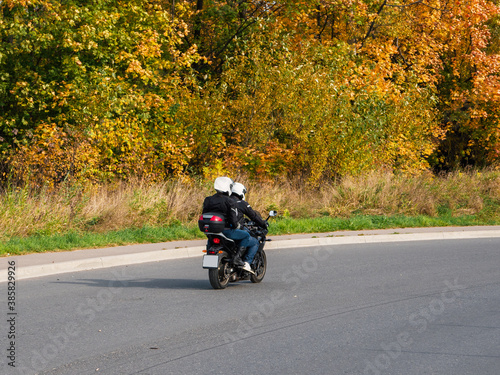 A couple of bikers on the same motorcycle rides on the autumn highway