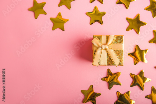 Gold box with a gift on a pink background. Gold stars confetti on a pink background. Golden gift and confetti close-up and copy space.