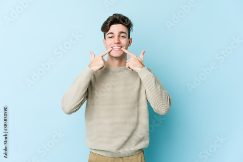 Young caucasian man isolated on blue background smiles, pointing fingers at mouth.