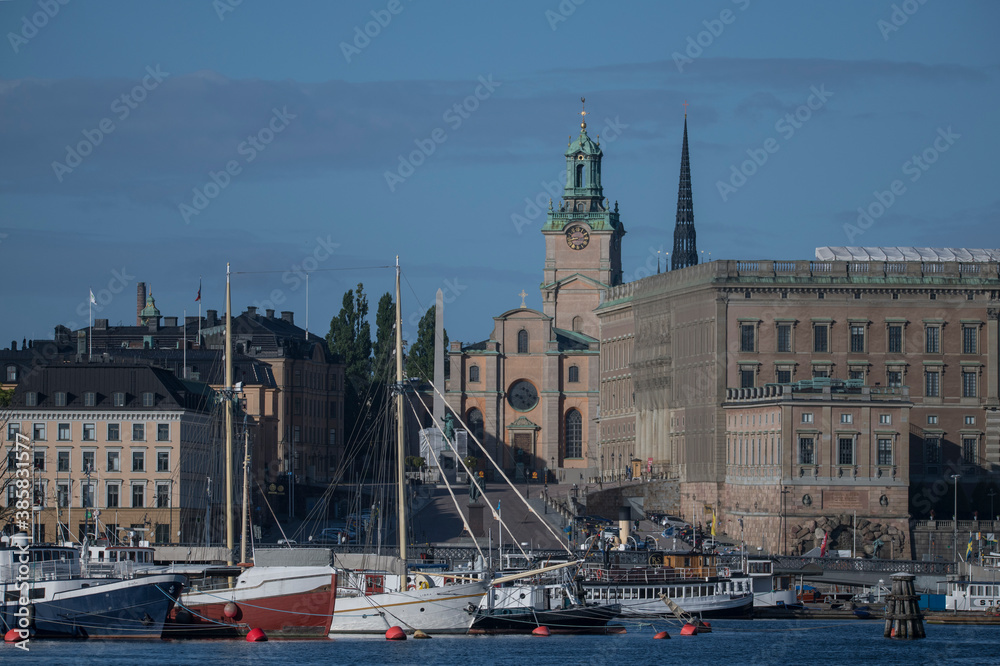 Fototapeta premium Boats at the jetties at the bridge between Blasieholmen and Skeppsholmen in Stockholm a sunny summer morning, old houses, the church Storkyrkan and the Royal Castle in the old town