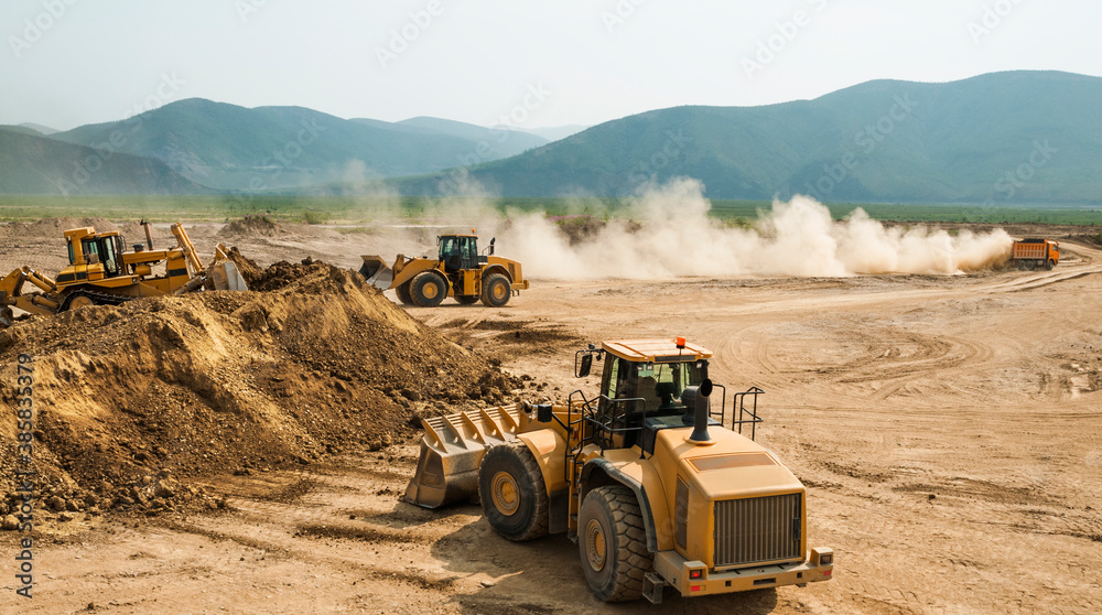 Earthworks in an open area on a summer sunny day. Cargo dump trucks, excavators, wheel loaders and bulldozers operate at the same time.