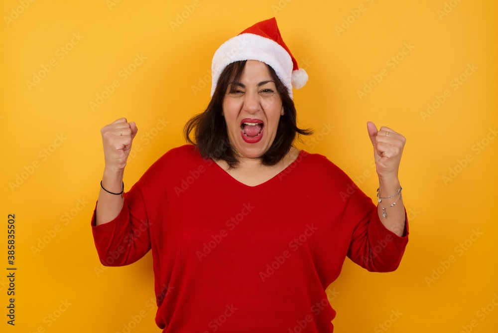 Waist up portrait of strong successful determined young female winner in casual t-shirt raising arms, clenching fists, exclaiming with joy and excitement. Victory, success and achievement concept.