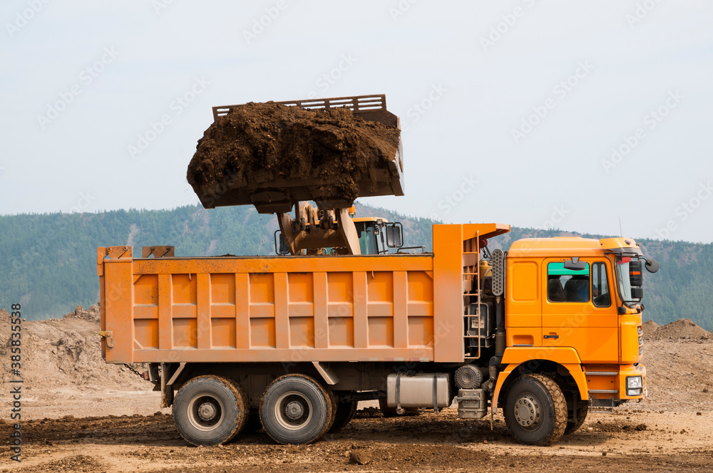 Obraz premium Wheel loader loads clay into the bucket of a dump truck