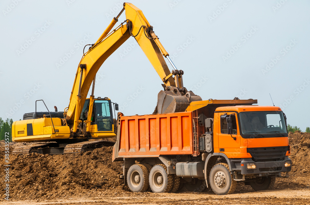 Excavator loads clay into the body of a dump truck on a sunny summer day Excavator loads clay into the body of a dump truck on a sunny summer day