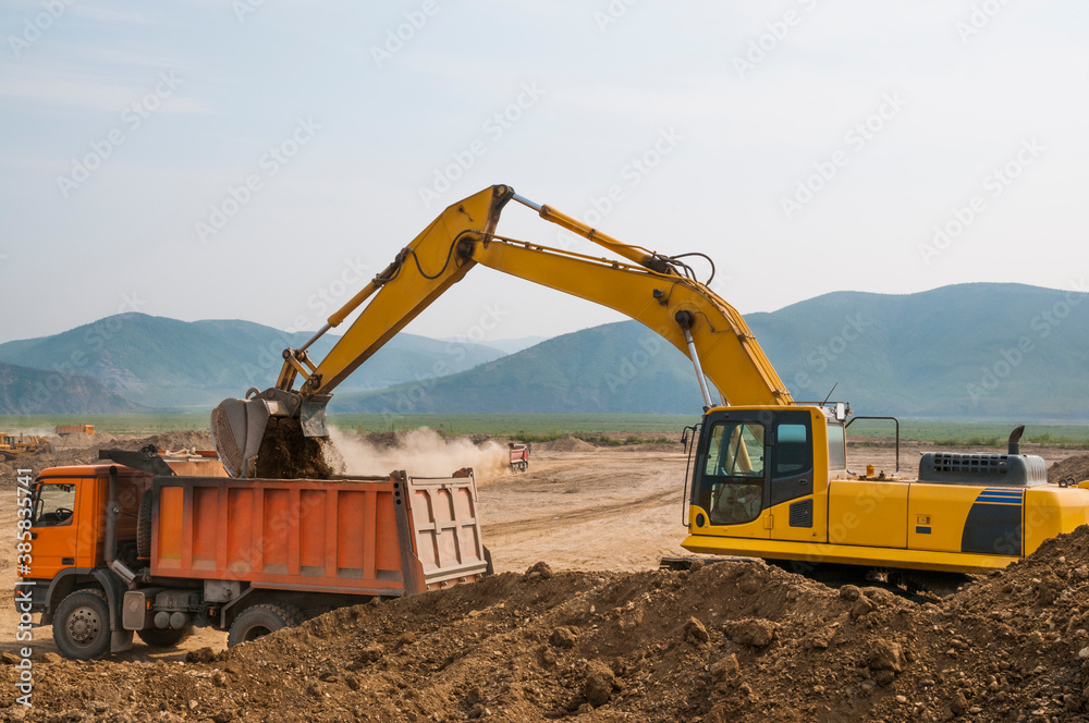 Excavator loads clay into the body of a dump truck on a sunny summer day