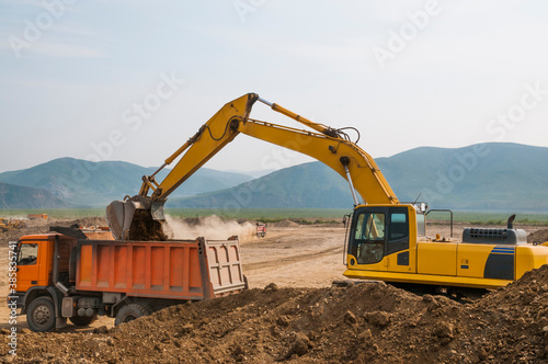 Excavator loads clay into the body of a dump truck on a sunny summer day