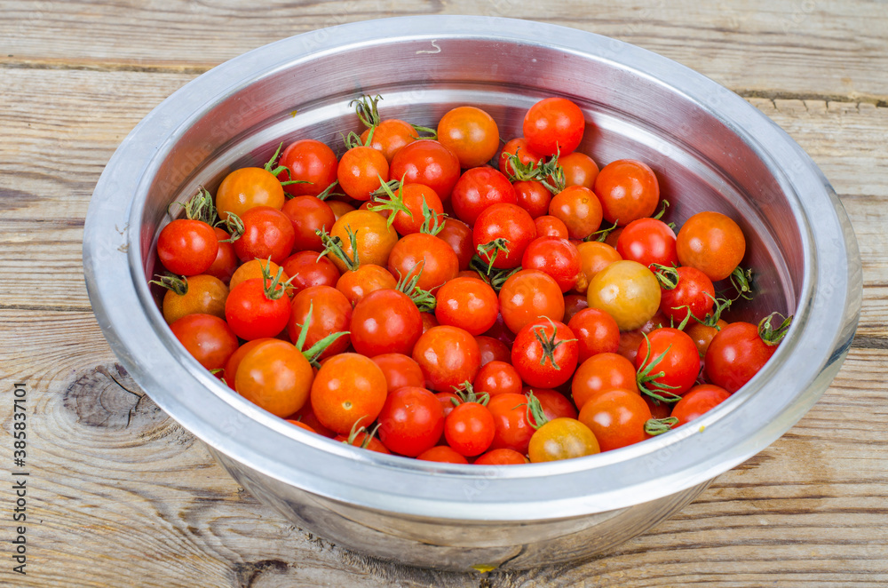 Small ripe red cherry tomatoes in metal bowl on wooden table Small ripe red cherry tomatoes in metal bowl on wooden table