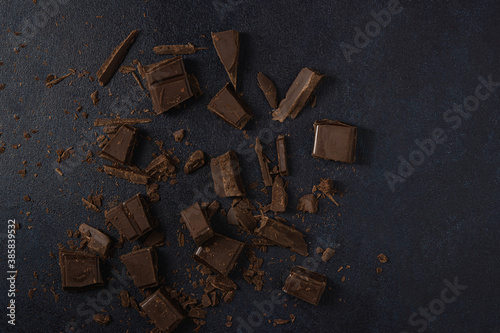 Dark chocolate broken into pieces isolated on a dark background. Top view, flat lay. Free space for text.