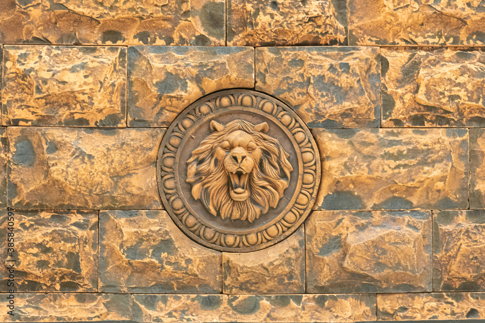 
A fragment of a wall tiled in the form of masonry with a bas-relief in the form of a lion's head. Background. Texture.