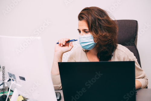 Beautiful caucasian female working in her office durgin coronavirus pandemic, wearing surgical mask photo