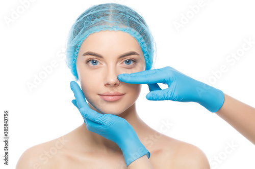 Young woman ready for rhinoplasty, doctor in blue gloves touching her nose, isolated on white background photo