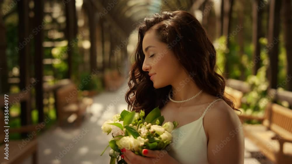 Gorgeous bride standing under arch. Beautiful woman smelling flowers in garden