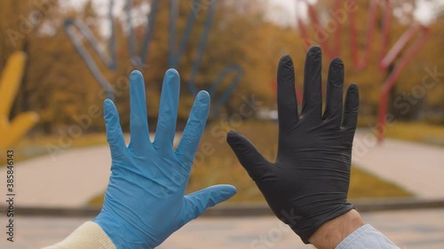 Close up male and female hands in a black and blue protective latex gloves against autumn trees. Yellow leaves on the trees. Rain drops falling on the gloves. Fall in the city park