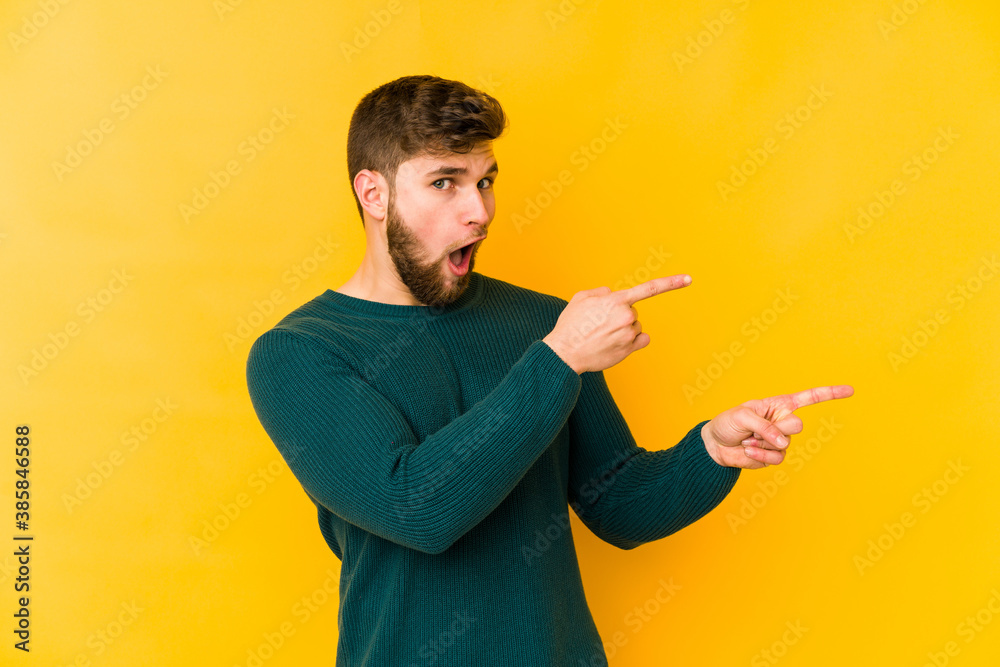 Young caucasian man isolated on yellow background pointing with forefingers to a copy space, expressing excitement and desire.