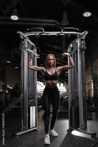 a girl of athletic physique trains in a fitness club to work out biceps in a crossover