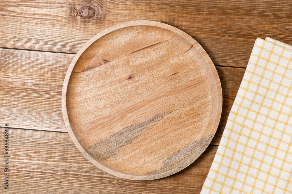 Blank round wooden plate and napkin on wood backdrop, top view.