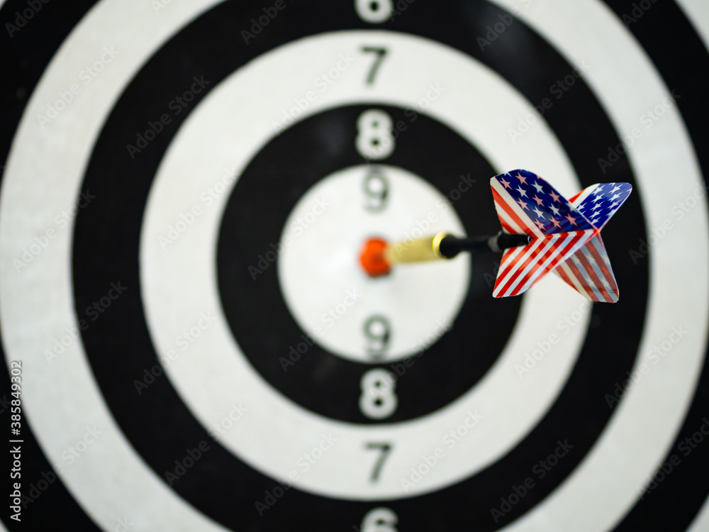 Dart arrow with tail of USA flag backgroun hitting in the target center of dartboard. Bullseye is a target of business. The concept of a successful strategy and business marketing. Dart arrow with tail of USA flag backgroun hitting in the target center of dartboard. Bullseye is a target of business. The concept of a successful strategy and business marketing.