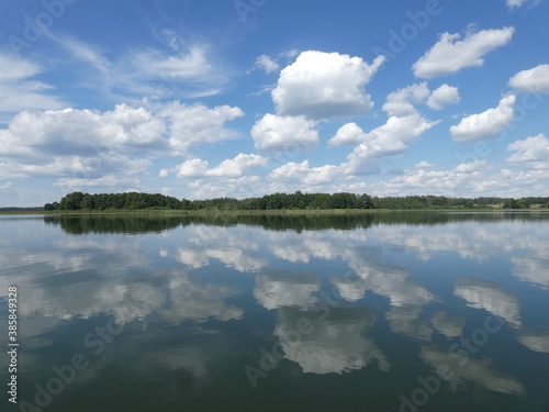 Scenic landscape with white clouds on blue sky and their reflection in the calm waters of Łaźno Lake, Mazury Province, Poland