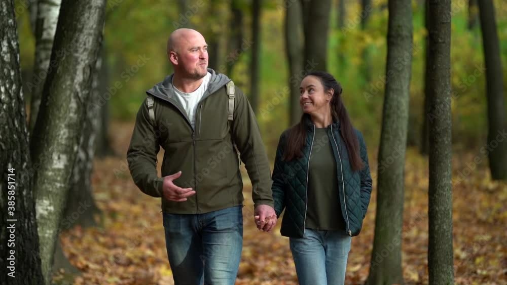 Happy adult couple walking through the autumn forest together by the hand and talking Happy adult couple walking through the autumn forest together by the hand and talking