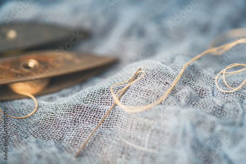 Closeup of Needle and Thread on Blue Fabric with Antique Tatting Shuttles in Background photo