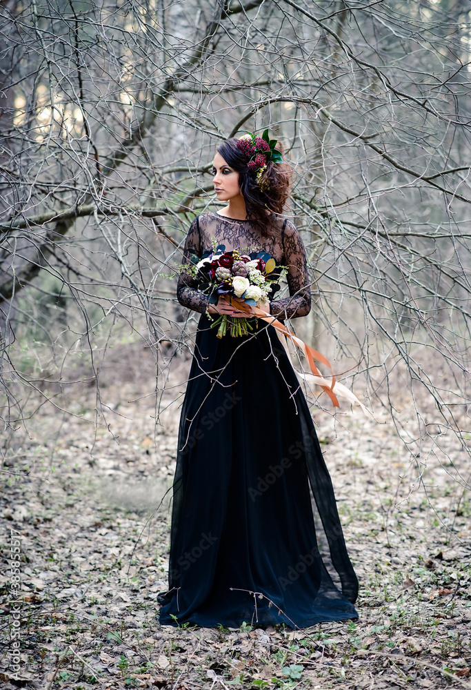 A Gothic woman in a black dress with a bouquet of flowers in a mysterious forest. Halloween concept. A Gothic woman in a black dress with a bouquet of flowers in a mysterious forest. Halloween concept.