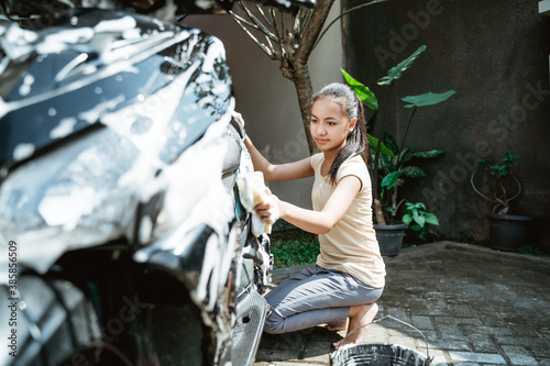 asian young girl washing his motorcycle scooter with soap and sponge at home