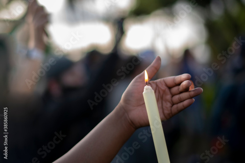 Black hand cups a candle flame at a peace vigil