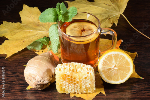 Autumn tea. A cup of hot tea with lemon, mint, and ginget on the table covered by autumn leaves photo