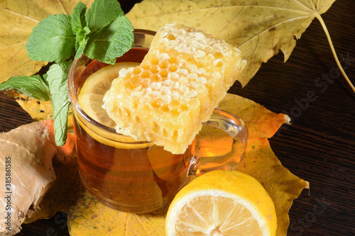 Autumn tea. A cup of hot tea with lemon, mint, and ginget on the table covered by autumn leaves photo