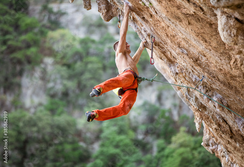 Young male rock climber after jumping and gripping small handholds