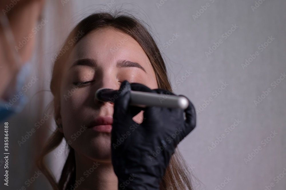 the process of applying makeup to a beautiful brunette by a master in a medical mask and black gloves. beauty, modeling and cosmetics concept. the process of applying makeup to a beautiful brunette by a master in a medical mask and black gloves. beauty, modeling and cosmetics concept.