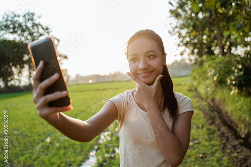 portrait of a beautiful young girl looking while holding a cellphone take a selfie on sunset photo