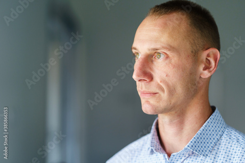 Front view close up portrait of male adult caucasian man with short blonde hair and green eyes standing at home in day looking to the side serious with copy space