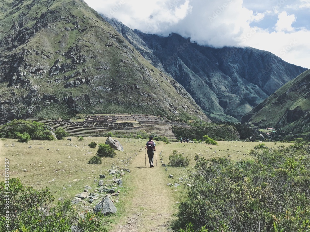 Hiking through an open field toward Inca Ruins at the base of a mountain. Inca Trail, Peru