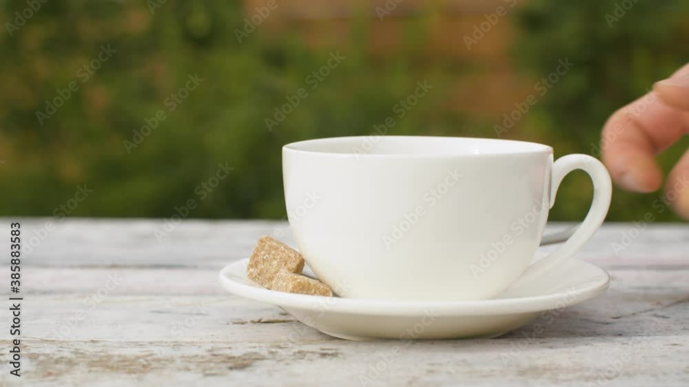 Close-up hand putting cup of hot tea on the table in the garden. Steam rises above the cup and is blown away by the wind. Dolly shot Close-up hand putting cup of hot tea on the table in the garden. Steam rises above the cup and is blown away by the wind. Dolly shot
