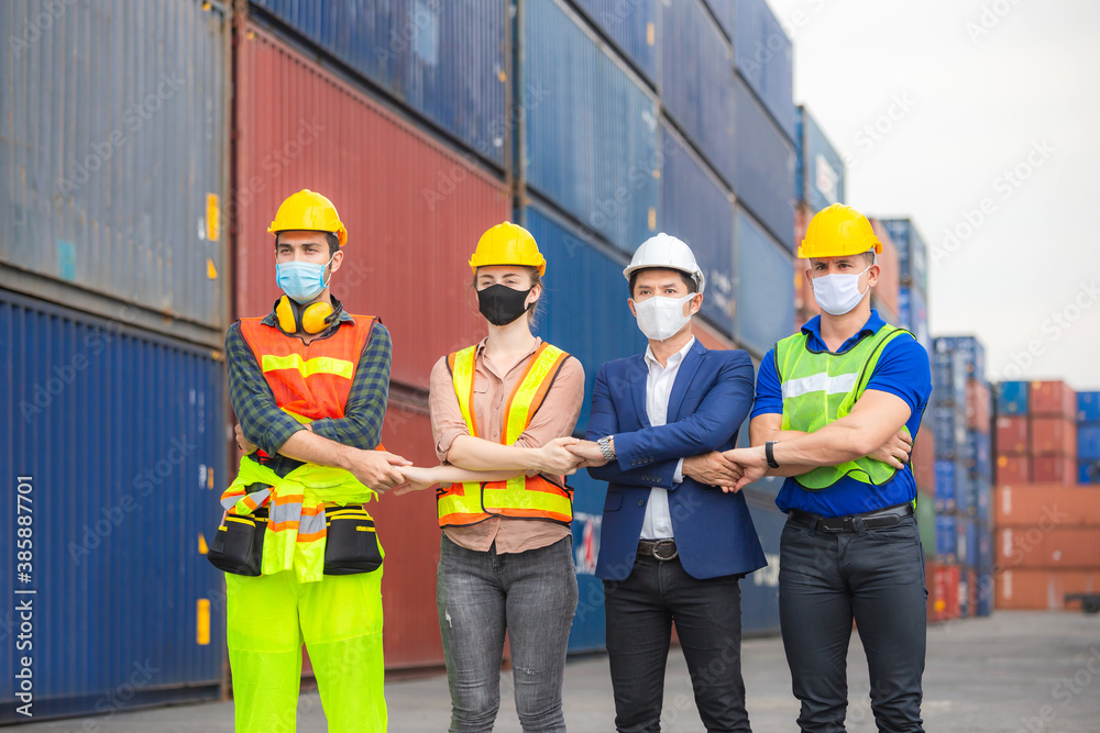 Factory worker and engineer team wearing protection face mask, Team holding hands and standing in row at cargo containers Factory worker and engineer team wearing protection face mask, Team holding hands and standing in row at cargo containers
